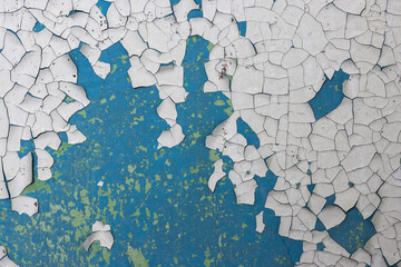 Peeling paint on the wall. Old concrete wall with cracked flaking paint. Weathered rough painted surface with patterns of cracks and peeling. Grunge texture for background and design. High resolution.