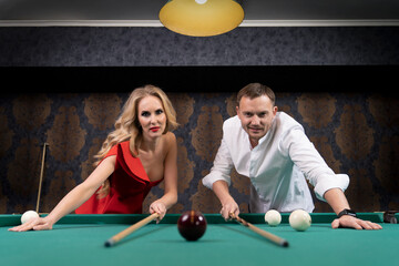 young man and sexy young woman bent over the pool table holding a wooden cue
