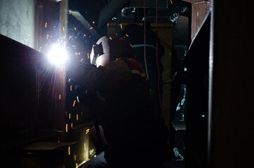 Obraz na płótnie Canvas Black Steel Metal Welder Worker Welding on a Vertical Position Using Torch for a Sparking Arc
