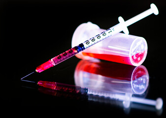 A syringe with a vial of red fluid is shown on a glass table