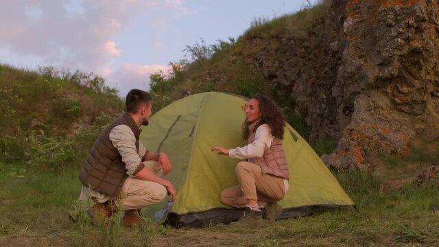 Young man and woman spending weekend evening together in nature finishing setting camp tent