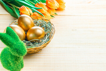Easter Golden colour eggs in basket with spring tulips, white feathers on wooden background in Happy Easter decoration. Festive decoration.