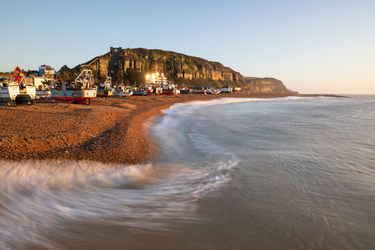 Fishing boats on beach at The Stade with breaking waves and East Hill behind at sunrise, Hastings, East Sussex