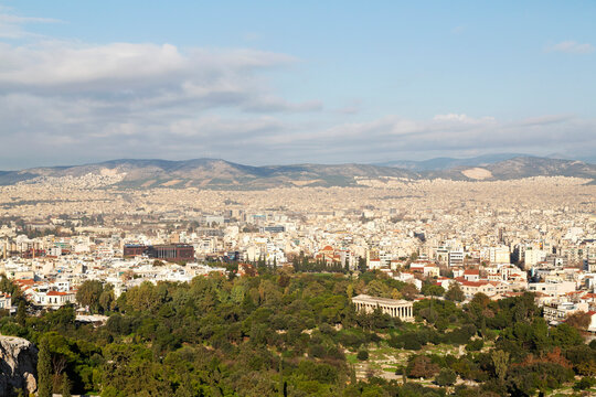 Temple of Hephaestus among trees on the ancient agora, in front of buildings of modern Athens, Greece