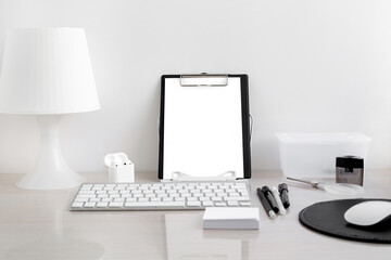 A white sheet of paper on a black folder in a bright room on the desktop. Notebook, self-adhesive notes, computer keyboard and pens in the workplace. Minimalistic design