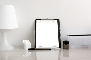 A white sheet of paper on a black folder in a bright room on the desktop. Notebook, self-adhesive notes, computer keyboard and pens in the workplace. Minimalistic design