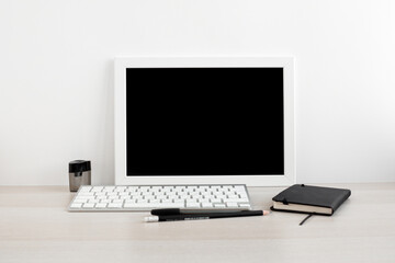 White frame with black background in a bright room on the desktop. Notebook, computer keyboard, and pens in the workplace. Minimalistic design