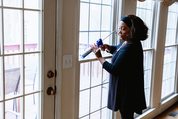 Senior woman weather sealing, caulking windows for winter