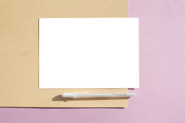 A blank layout of a white sheet on an abstract pink and beige table illuminated by the sun. The concept of minimalism and modernity. White pen under the sheet.