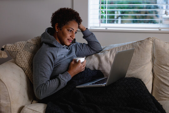 Black woman drinking tea on couch snuggled and warm
