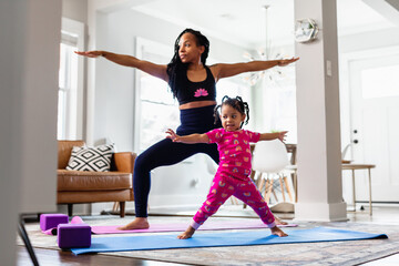 Black Mother and daughter doing yoga in family room, warrior pose