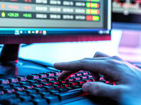 Hands of trader typing on keyboard in front of computer monitor displaying stock market data
