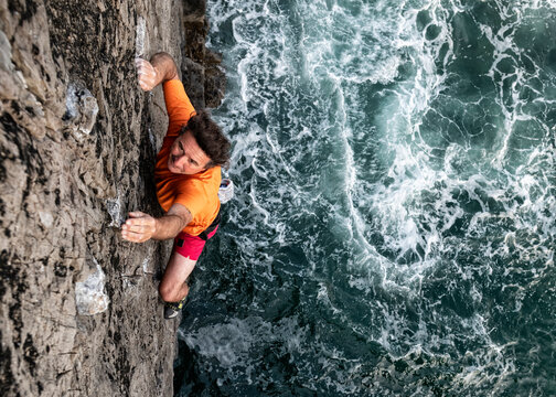 Passionate male rock climber climbing rocky cliff by sea