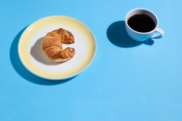 A plate with a croissant and a cup of coffee on a blue background. Pop style. With space for text