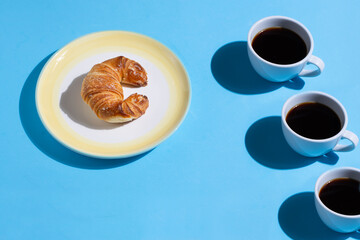 A plate with a crescent and three cups of coffee forming a pattern on a blue background. Pop style. With space for text.
