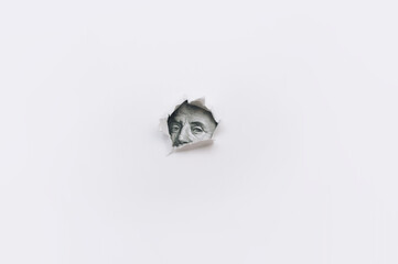 Portrait of Benjamin Franklin from a hundred dollar bill in a torn rounded hole in white paper. The...