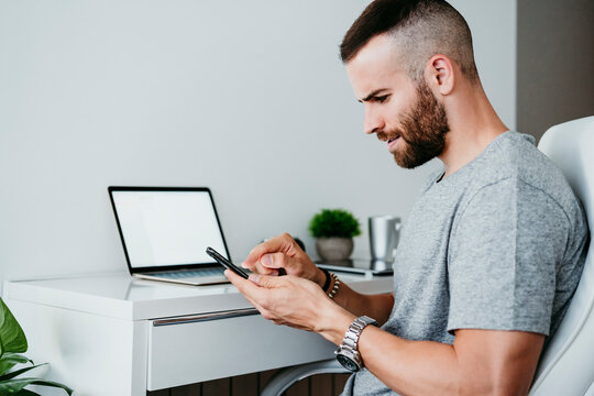 Young man working on mobile phone and laptop at home