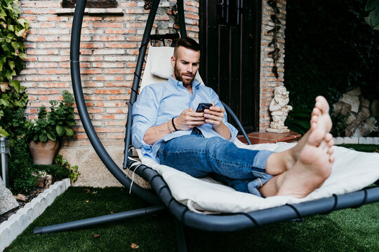 Young man working with mobile phone while sitting in hammock on terrace