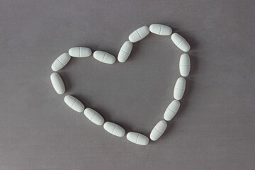 Pills are laid out in the shape of a heart on a gray background. With copy space
