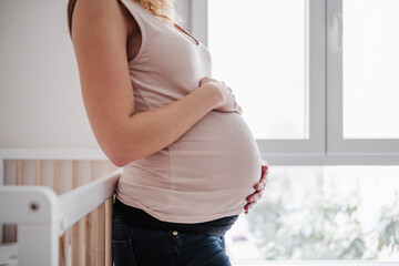 Pregnant woman with hands on stomach standing by window at home