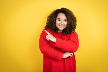 Young african american woman wearing red sweater over yellow background smiling and pointing with hand and finger to the side