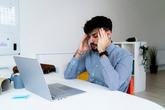 Tired businessman rubbing temples at desk in creative office