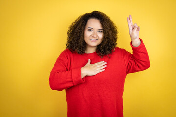 Young african american woman wearing red sweater over yellow background smiling swearing with hand...