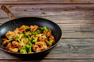 Spicy chicken teriyaki with broccoli in pan on wooden background.
