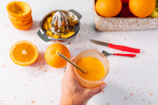 Woman holding orange juice glass with drinking straw over modern terrazzo marble - Powered by Adobe