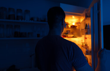 Man looking for food in refrigerator at night.