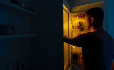 Man looking for food in refrigerator at night.