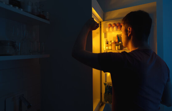 Man looking for food in refrigerator at night.