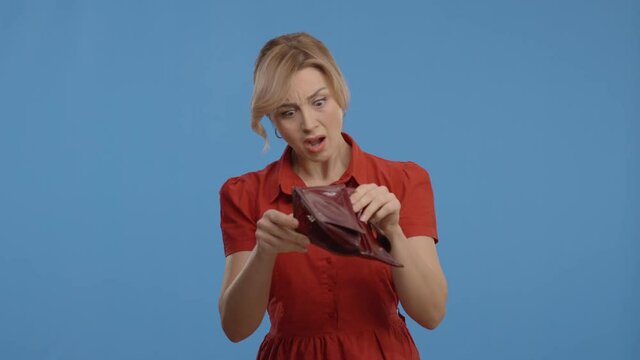 Against the blue background, the young woman is surprised to see that there is no money in her wallet. The woman shakes her empty wallet. Empty wallet, correct spending concept.Slow motion video.