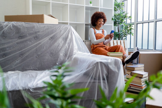 Smiling Afro woman using mobile phone while moving in new loft apartment