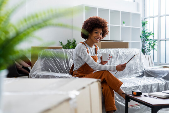 Smiling woman having coffee while holding checklist on clipboard in new home