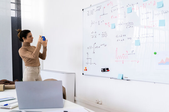 Female student taking photograph of math whiteboard while standing at home
