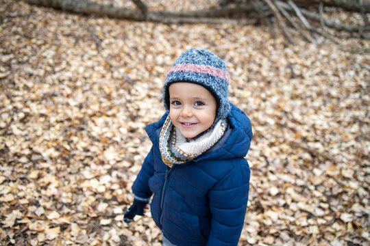 Cute boy wearing warm clothing standing on autumn leaves in forest