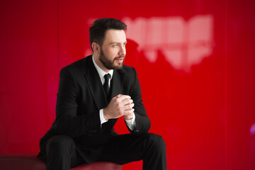 Young businessman with a beard dressed in a black classic suit on a red background