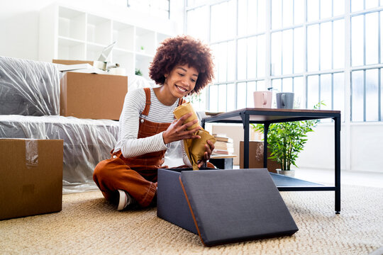 Smiling Afro woman keeping wrapped glasses in box while moving into new house