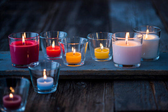 Colorful glass candles burning on wooden surface