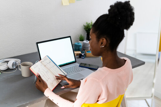 Young fashion designer analyzing diagram in book while working at home office