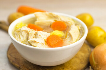 Chicken Soup stew broth and vegetables in white bowl on old rustic wooden cutting board. Close up. Selective focus. Copy space
