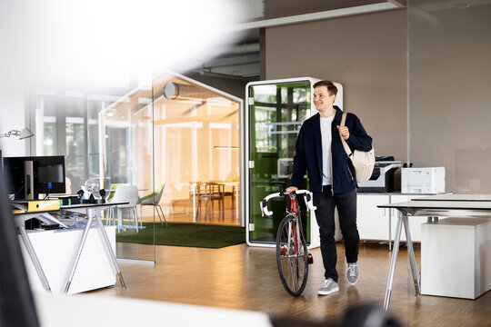 Smiling businessman walking with bicycle at open plan office