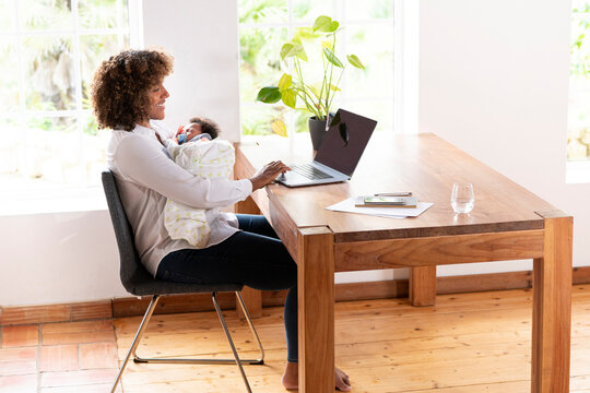 Mid adult woman holding baby while working on laptop at home