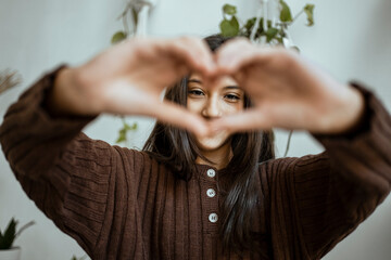 Girl in warm clothing showing heart shape with hand at home