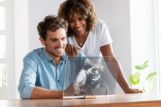 Happy couple checking ultrasound image over transparent screen at home