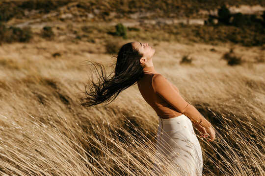 Carefree woman standing amidst grass in field during windy day