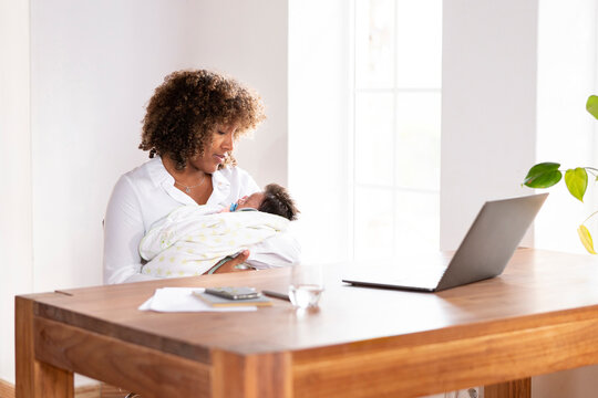 Mother looking at sleeping baby while sitting by table at home office