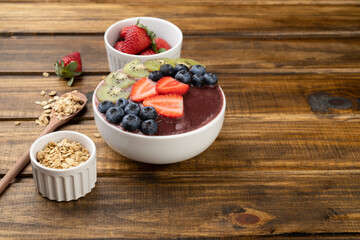 Brazilian typical acai bowl with fruits and muesli over wooden background with copy space