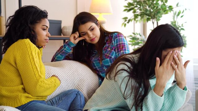 Multiethnic Women Sitting On Sofa And Talking, Their Roommate Feeling Stressed And Closing Face With Hands. Friends Expressing Sympathy And Trying To Calm Her Down. Concept Of Support